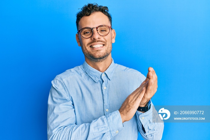 Young hispanic man wearing casual clothes and glasses clapping and applauding happy and joyful, smiling proud hands together