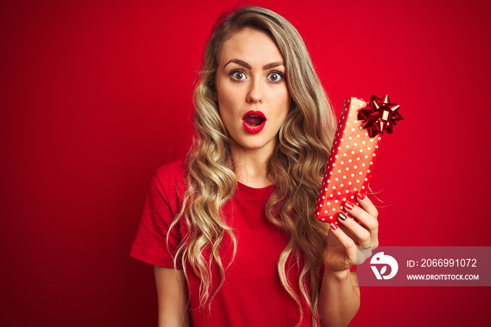 Young beautiful woman holding valentine gift over red isolated background scared in shock with a surprise face, afraid and excited with fear expression