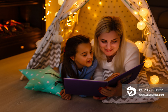 Mom with child reading book and relaxing by the fire place some cold evening, winter weekends, cozy scene