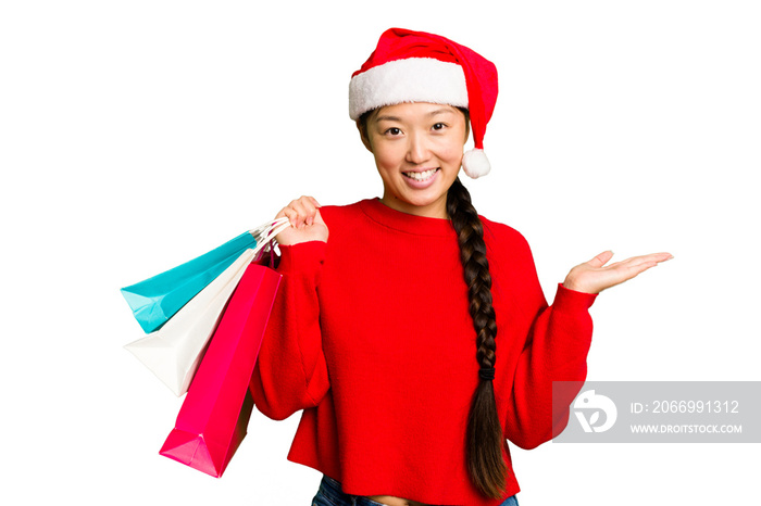 Young asian woman shopping a christmas presents isolated Young asian woman shopping a christmas presents isolated showing a copy space on a palm and holding another hand on waist.