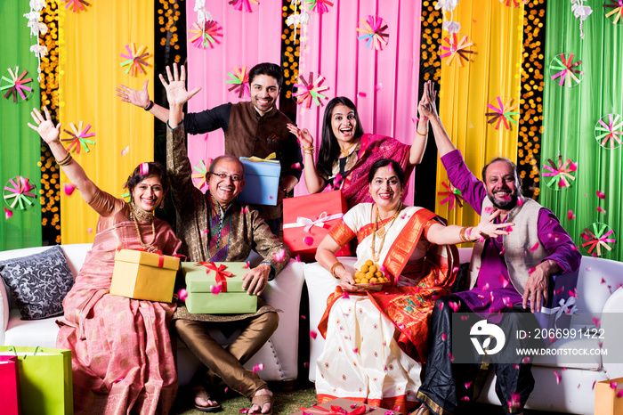 Indian Family posing for group photo on festival or wedding night, sitting on couch or round table with background decorated with colourful frills and lighting series