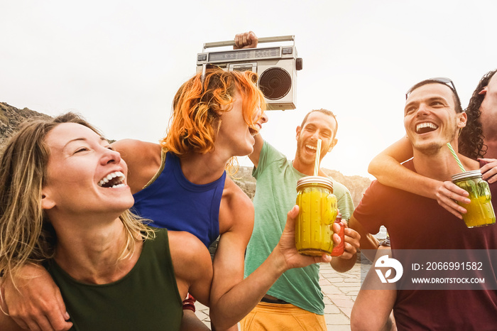 Happy friends having fun listening music with vintage boombox stereo outdoor while drinking cocktails on the beach - Party concept - Main focus on right man