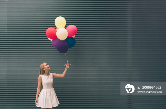 Happy young woman with colorful balloons on a street near the gray - outdoors summer concept