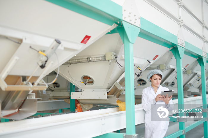 Wide angle portrait of  young woman standing by machines and using digital tablet while inspecting production at food factory , copy space