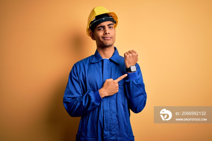 Young handsome african american worker man wearing blue uniform and security helmet In hurry pointing to watch time, impatience, looking at the camera with relaxed expression