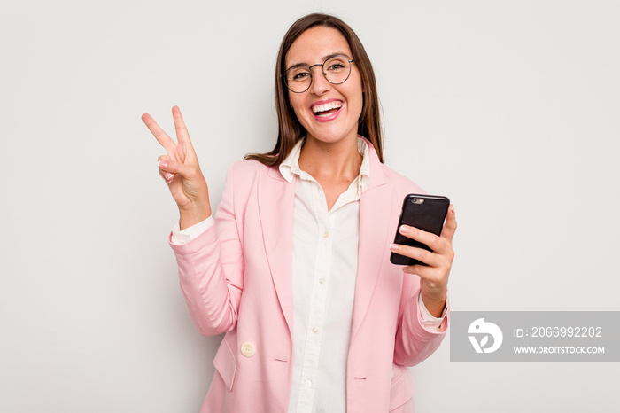 Business caucasian woman holding a mobile phone isolated on white background joyful and carefree showing a peace symbol with fingers.