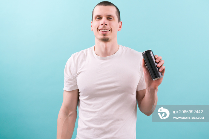 A man in a white t-shirt smiles and holds an empty black aluminum can on a blue background. Emotional. Failure. Feeling. Formal. Camera. Caucasian. Adult. Blur. Anger. Carefree. Furious