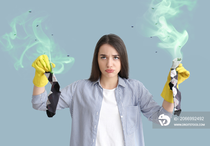 Displeased young woman with dirty stinky socks on color background