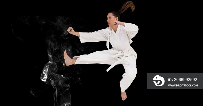Composition of female martial karate artist with white belt in the air over smoke and copy space