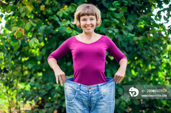 Young woman wearing big loose jeans with apple in hand - weight loss concept