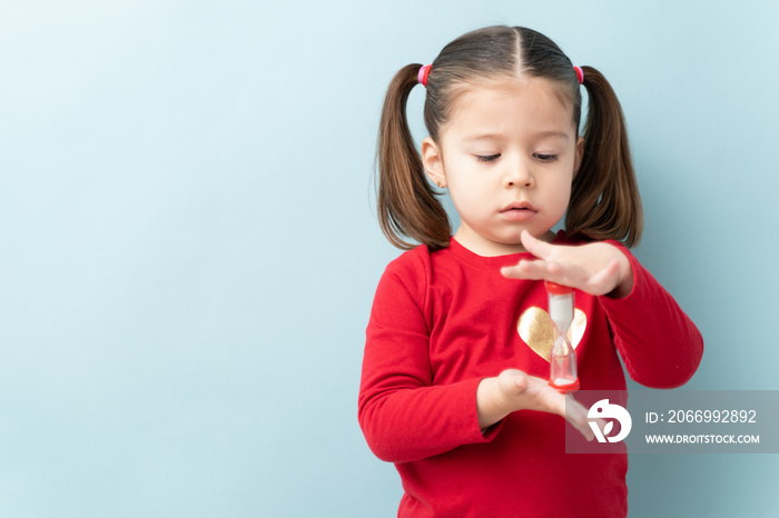 Serious looking little girl looking at a sand timer while practicing self-control during timeout in a studio with copy space