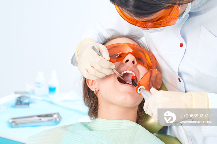 Girl child at the doctor. Dentist places a filling on a tooth with dental polymerization lamp in oral cavity. over clinic background