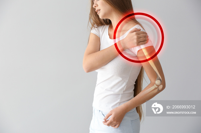 Young woman with pain in shoulder on light background