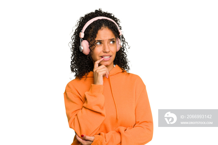 Young Brazilian woman listening to music with headphones isolated relaxed thinking about something looking at a copy space.