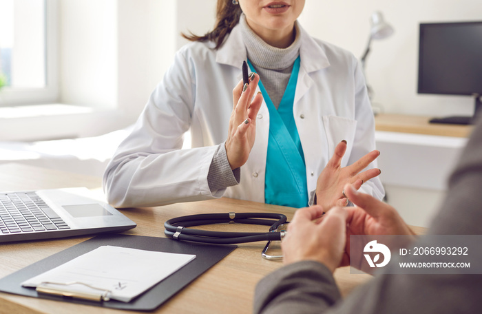 Patient having consultation with doctor. Professional physician at clinic or hospital sitting at desk with laptop, prescription and stethoscope and talking to her patient. Close up. Medical concept