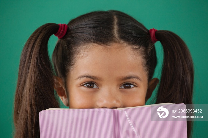 Schoolgirl hiding behind a book against green background