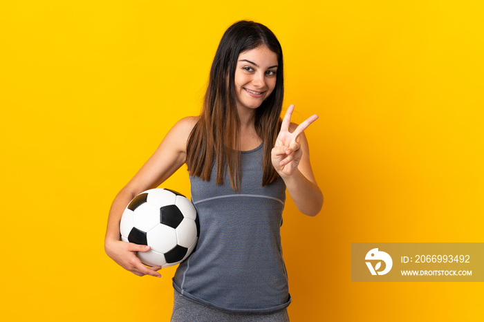 Young football player woman isolated on yellow background smiling and showing victory sign