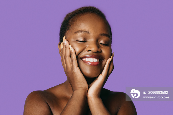 Nude african-american woman portrait, close eyes enjoying result after mask peeling scrub cream lotion, isolated on purple background. Healthy hair. Afro