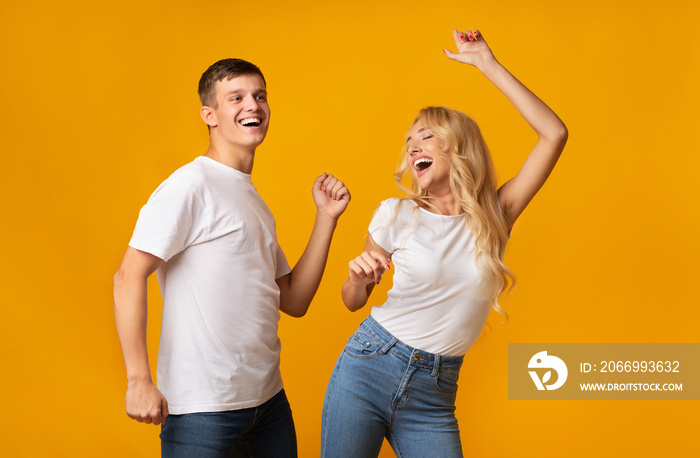 Joyful millennial guy and girl dancing over yellow studio background