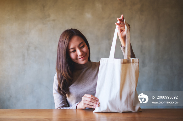 Closeup image of a beautiful young asian woman holding and carrying a white fabric tote bag for reusable and environment concept