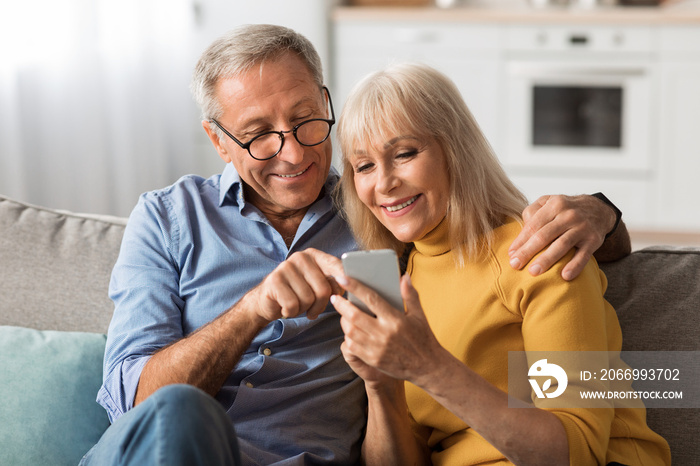 Happy Senior Couple Using Mobile Phone Together At Home