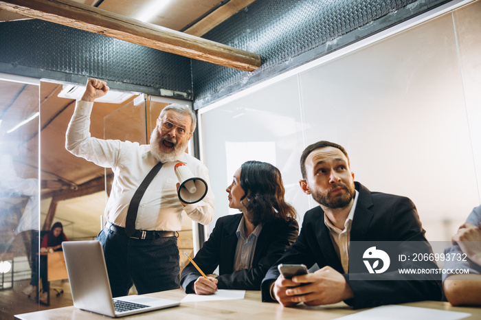 Shouting. Angry boss with megaphone screaming at employees in office, scared and annoyed colleagues listening at the table stressed out. Funny meeting, business, office concept. Screaming mad.