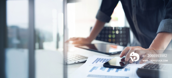 Business man using mobile phone, working at office with laptop computer and financial report graph data documents on desk