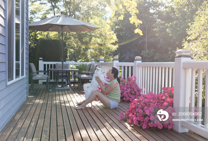 Woman and her pet dog outdoors on home deck during bright sunlight on a lovely summer morning