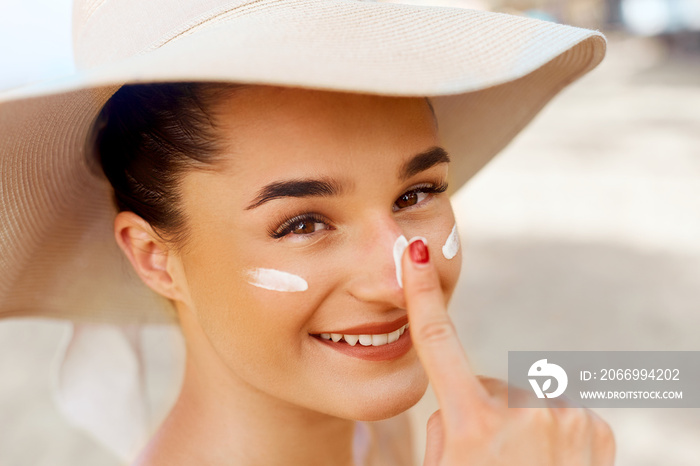 Beautiful Young woman with sun cream on face.  Female in hat applying  moisturizing lotion on skin.Skin care. Sun protection. Suntan