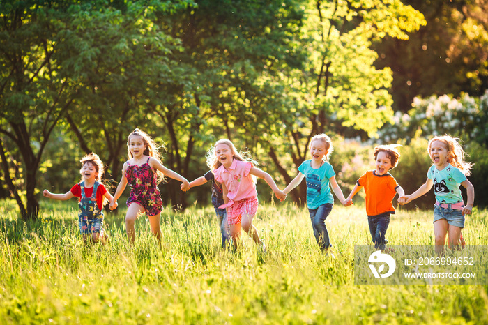 Large group of kids, friends boys and girls running in the park on sunny summer day in casual clothes .