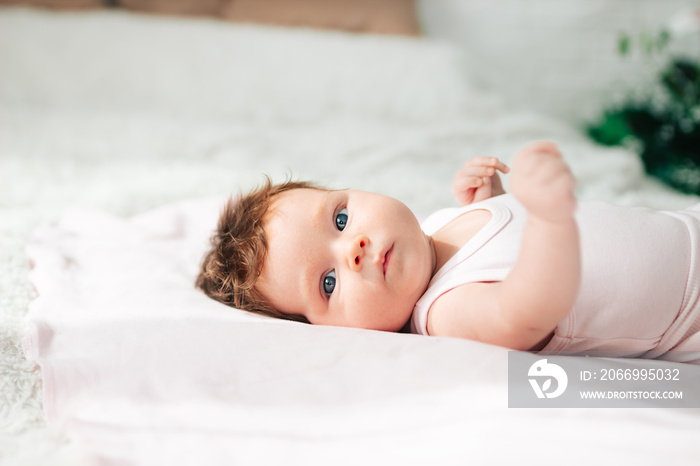 A newborn baby is lying on a snow-white bed. A beautiful child of European appearance. Healthy sleep, wakefulness, and waking up in the morning.