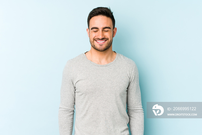 Young caucasian man isolated on blue background laughs and closes eyes, feels relaxed and happy.