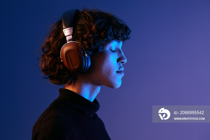 Man wearing headphones listening to music with his eyes closed, enjoying the sound, hipster lifestyle blogger, portrait purple background, mixed neon light, fashion style and trends, copy space