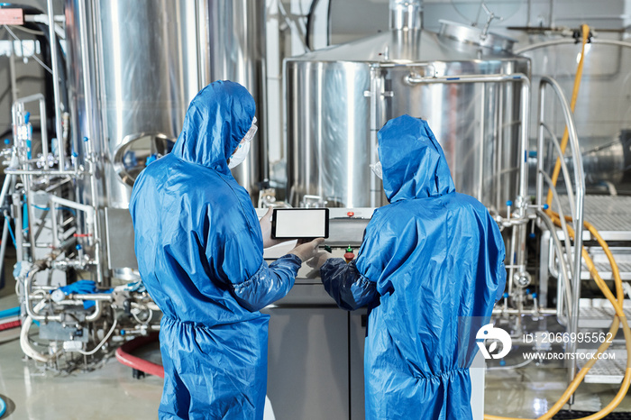 Back view of two workers using control panel at chemical factory