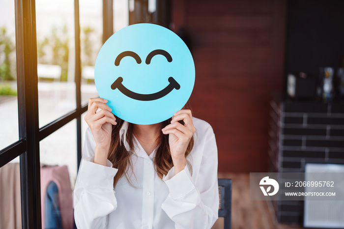 Asian woman holding blue happy smile face on paper cut, user giving good feedback rating, think positive , customer review, assessment, of mental health day, Compliment Day, satisfaction concept.