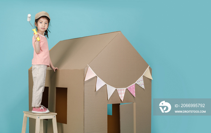 Asian little child girl painting her cardboard house isolated on blue long banner with copy space for your text, Creative at home with family concept