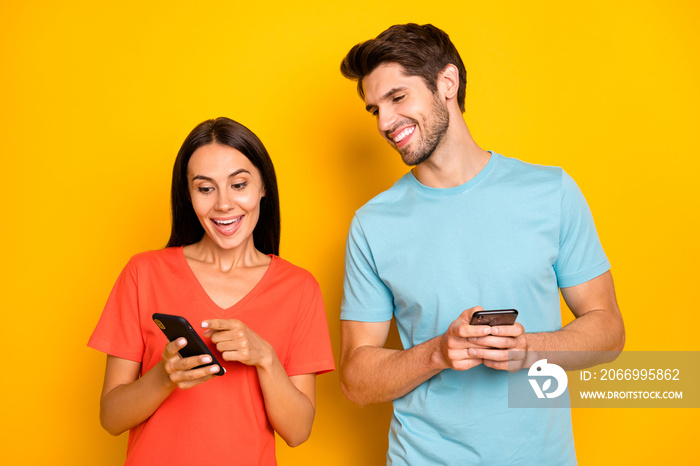 Photo of two funny guy lady people couple hold telephones showing finger positive comments reposts excited wear casual blue orange t-shirts isolated yellow color background