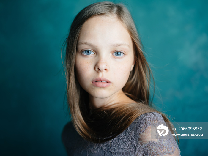 Portrait of a beautiful little girl in a gray dress on a blue background close-up cropped view of the model