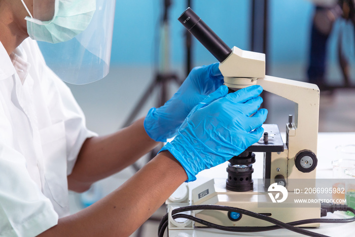 Indian Scientist man look into Microscope research in science laboratory. Asian biochemistry scientist using microscope in laboratory chemistry labs. Covid-19 medical research scientific experiment