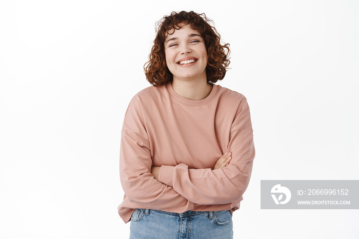 Beautiful caucasian woman with curly hair, cross arms on chest, laughing and smiling carefree, looking upbeat, standing against white background