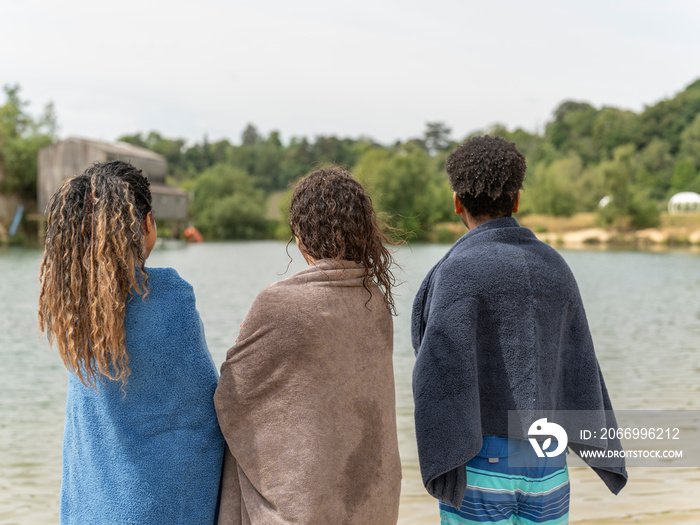 Friends wrapped in towels looking at lake