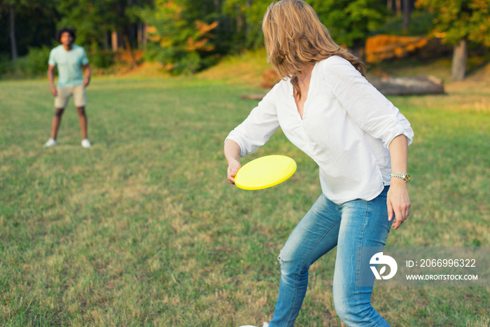 Mixed race couple throwing frisbee on the summer meadow