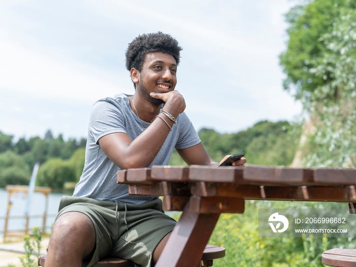 Young man using phone while sitting by lake