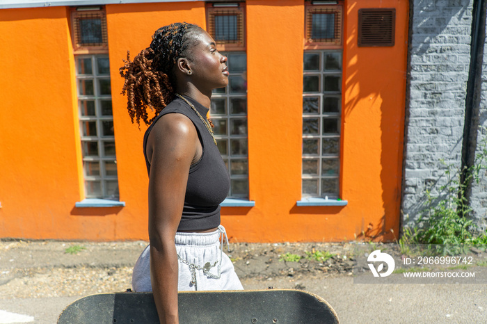 Young woman walking outdoors carrying skateboard