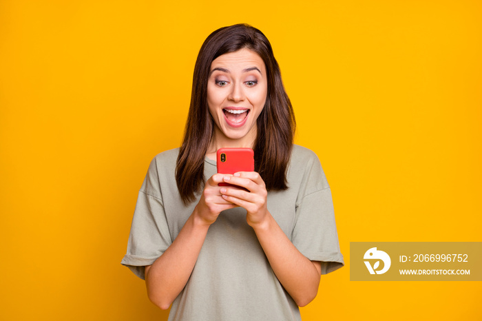 Portrait of lovely cheerful focused brown-haired girl using device having fun isolated over bright yellow color background