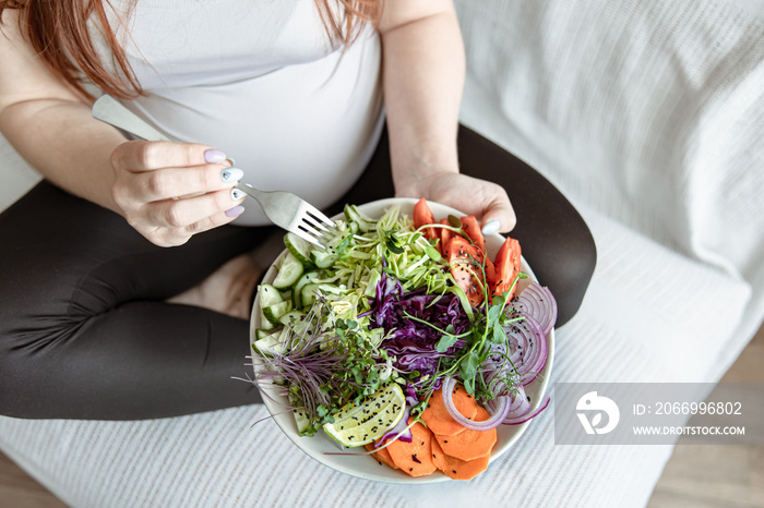 Close-up of a pregnant woman eating a bright fresh vegetable salad.