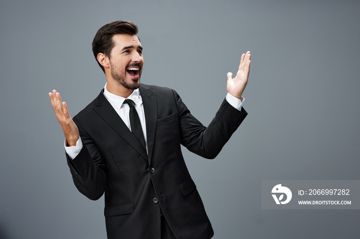 Man businessman surprised smile with teeth and raised his hands up happy in a business suit on a gray background with a brunette beard