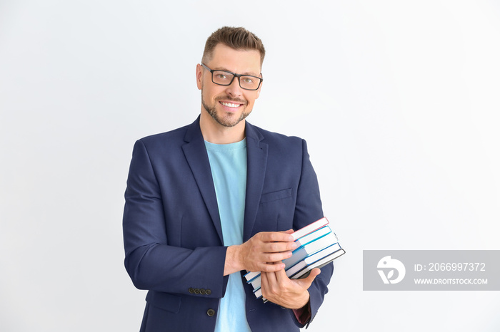 Handsome male teacher with books on light background