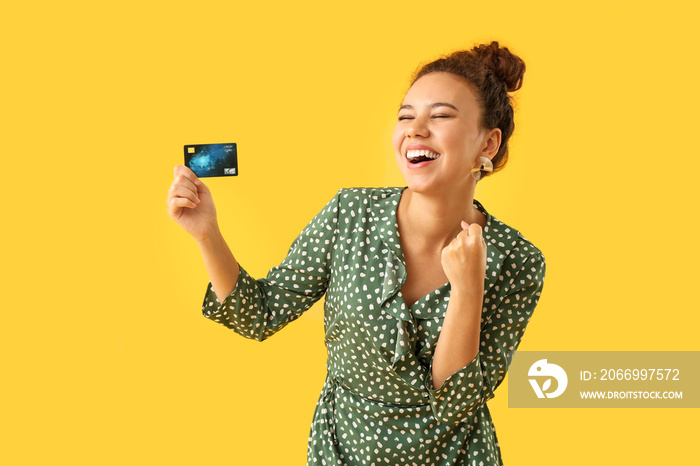 Happy African-American woman with credit card on color background