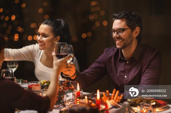 holidays, party and celebration concept - multiethnic group of happy friends having christmas dinner at home and drinking wine